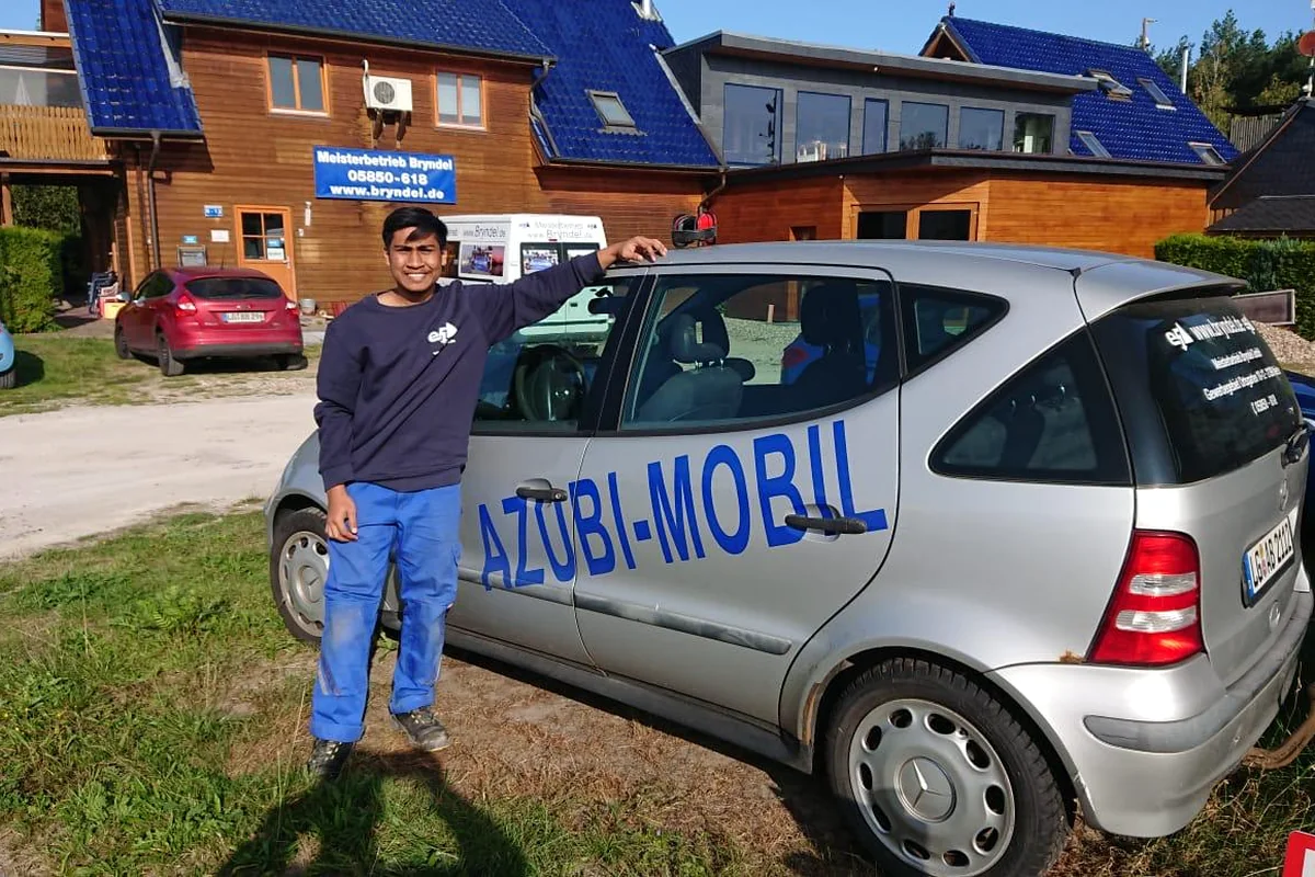 Auszubildender vor einem deutschen Ausbildungsbetrieb neben einem Azubi-Mobil